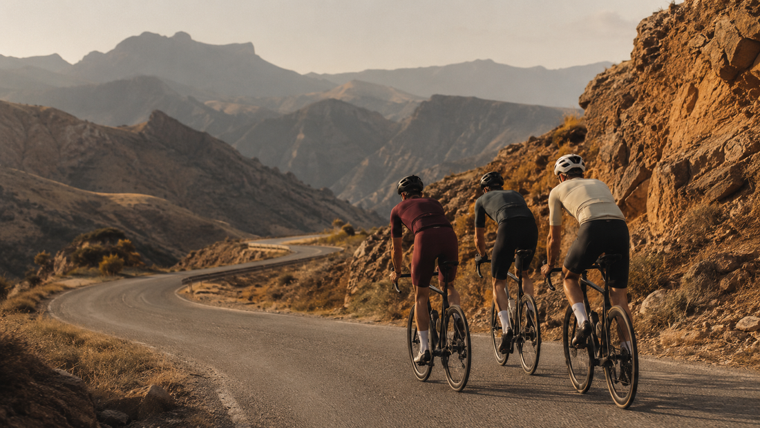 Three amateur road cyclists climbing a switchback mountain road through arid Spanish mountains in golden evening light, echoing the Vuelta a España 2026 mountain stages